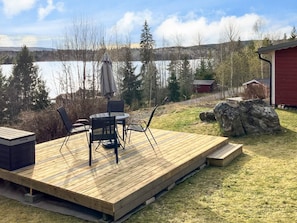 A wooden deck with outdoor furniture, a lake view, and a red building in the background.
