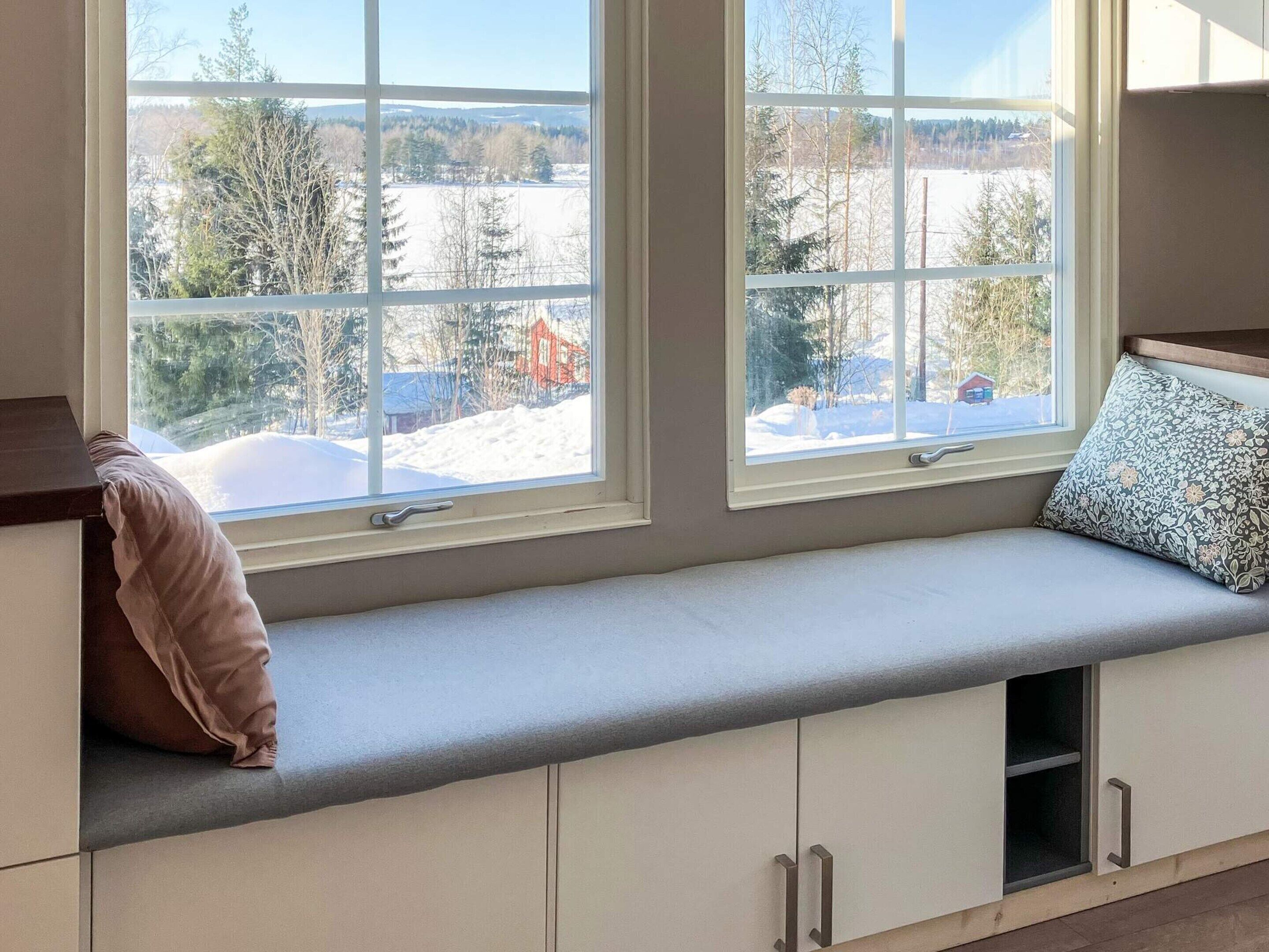 A room with a built-in bench seat with storage cabinets underneath, large windows with a view of a snowy landscape.