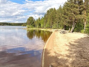 A lakeside beach with a picnic table and a row of trees. - 4 Person Holiday Home in Enviken (Enviken)
