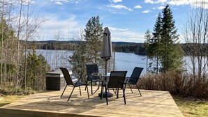 Une terrasse en bois, dotée de mobilier d’extérieur et d’une table, qui offre une vue sur un lac.