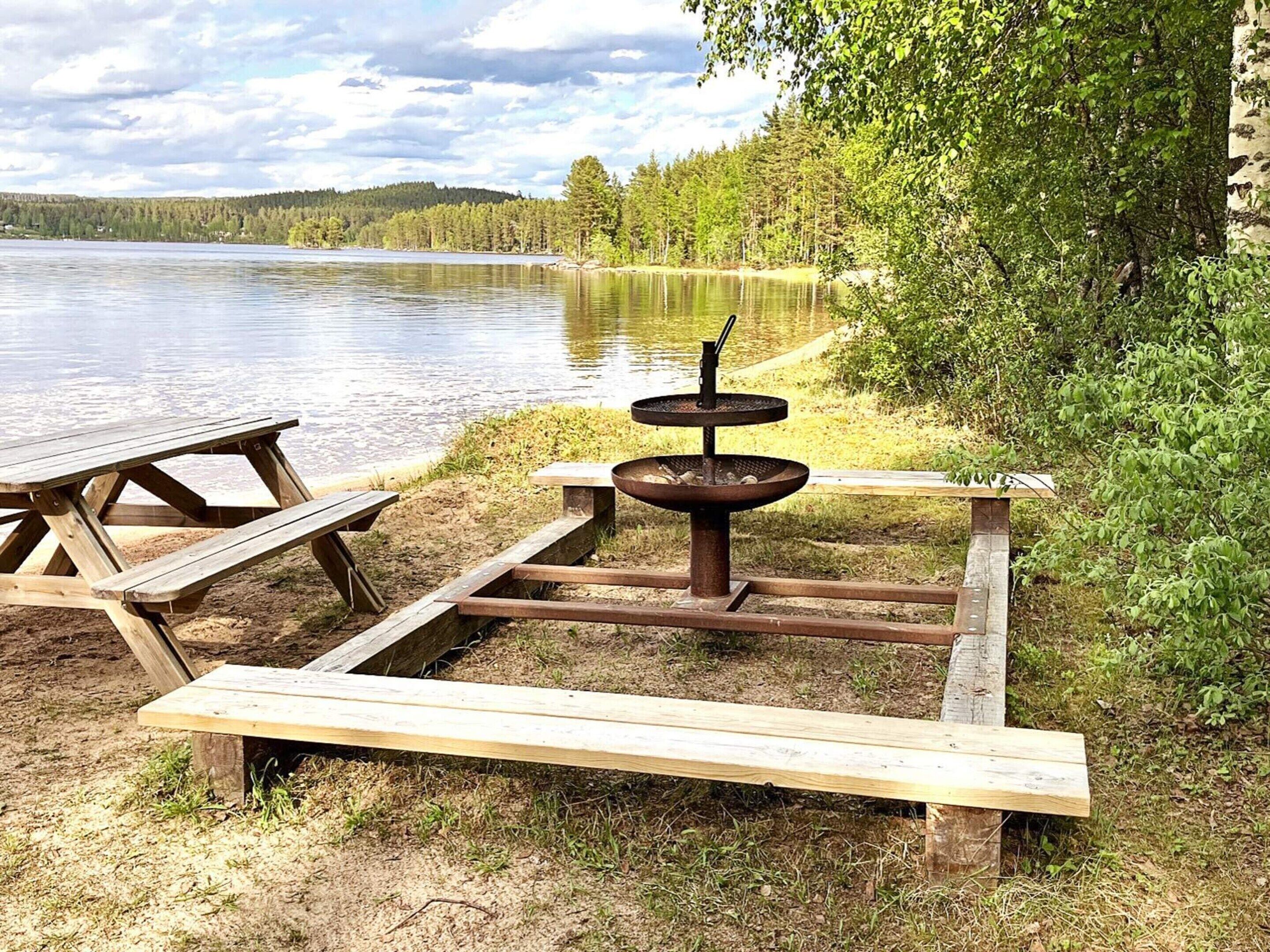 Ein Picknickplatz am Seeufer mit einer Holzbank, einem Picknicktisch und einer Feuerstelle.