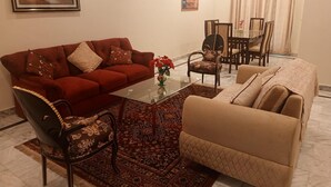 A living room with a red sofa, a beige sofa, a glass coffee table, and patterned chairs. There is a dining area with a table and chairs in the background. - Impeccable 3-bed Apartment in Lahore (Lahore)