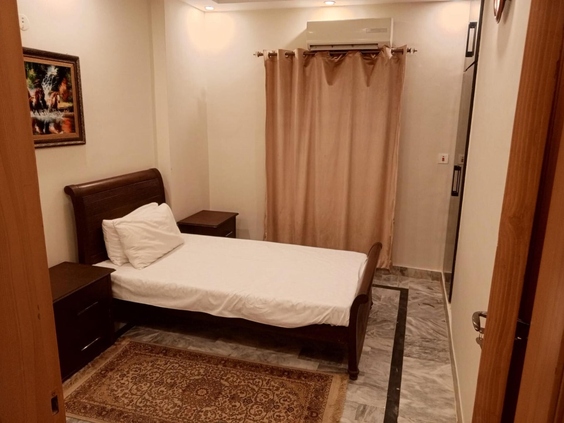 Ein ordentlich eingerichtetes Schlafzimmer mit Bett, Nachttischen, einem Teppich und einem Vorhang.