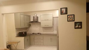 A compact kitchen with light-colored cabinets, a gas stove, a range hood, and a refrigerator. There are framed pictures on the wall. - Impeccable 3-bed Apartment in Lahore (Lahore)