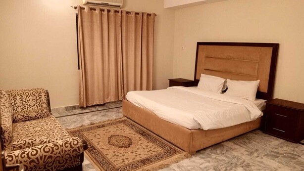 A bedroom with a bed, a chair, a nightstand, an air conditioner, and a window with curtains. - Impeccable 3-bed Apartment in Lahore (Lahore)