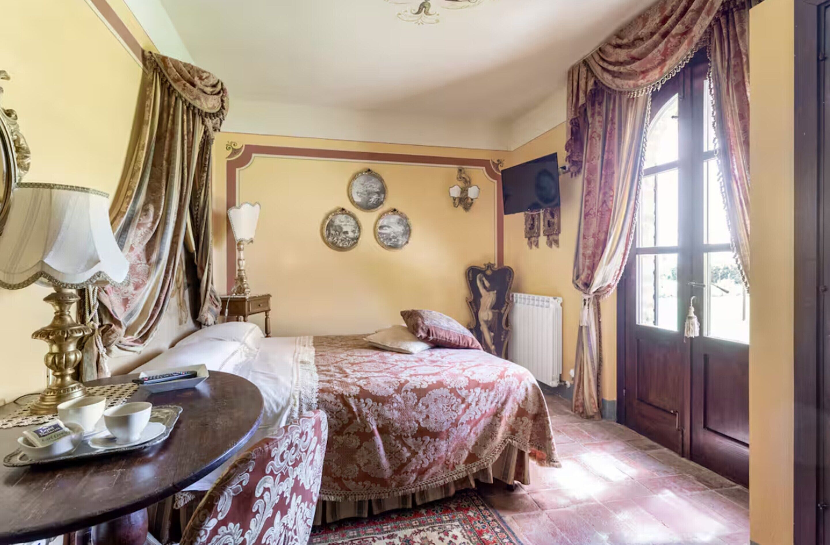 Ein traditionell eingerichteter Raum mit Bett, Tisch mit Tablett, Lampe und einem fenster mit Vorhängen.