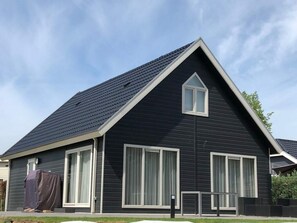 Uma casa moderna de dois andares com fachada escura, detalhes em branco e telhado íngreme.