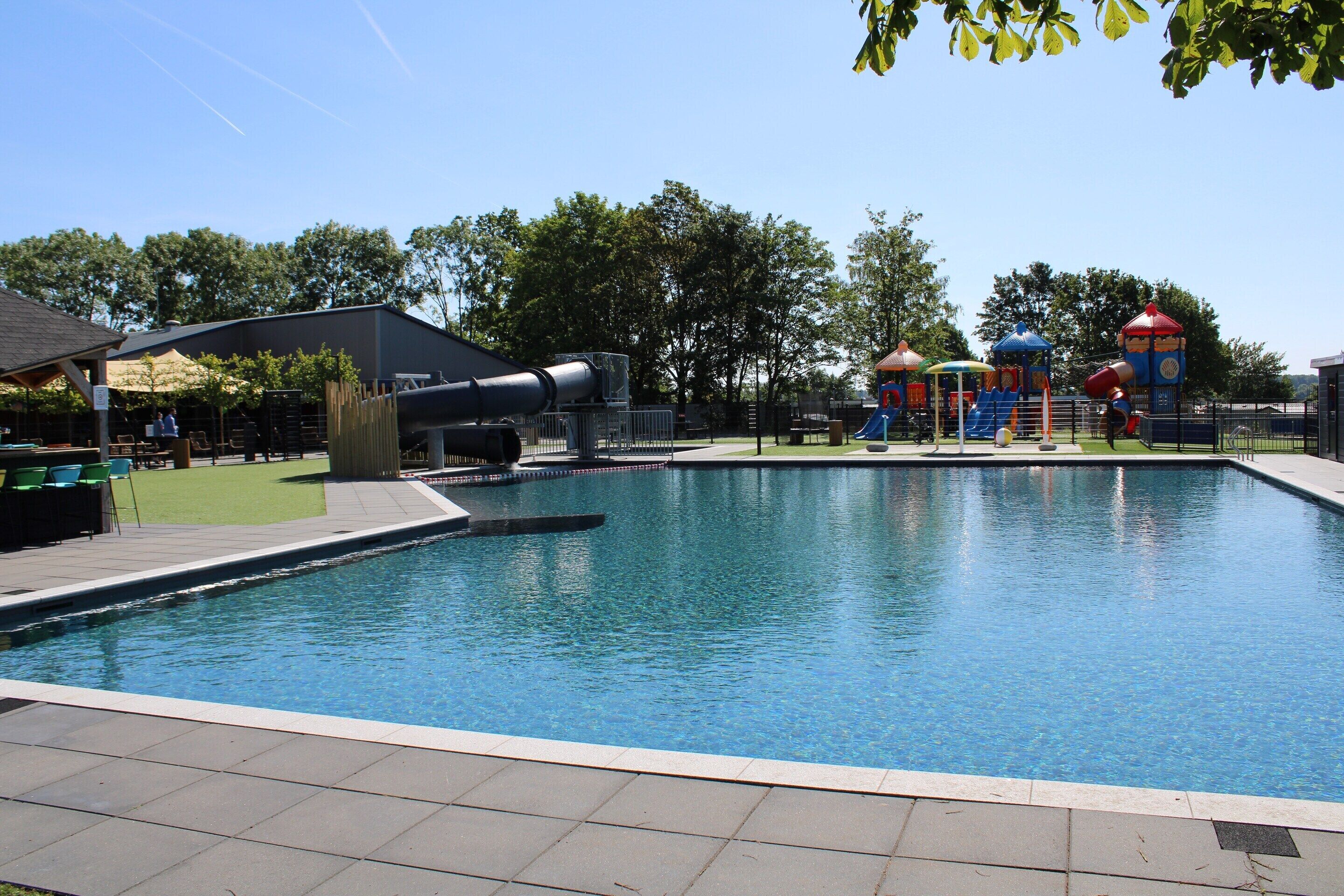 A swimming pool with a water slide and play structures in the background.