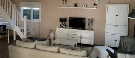 A living room with a sofa, TV, white cabinet, and a staircase.