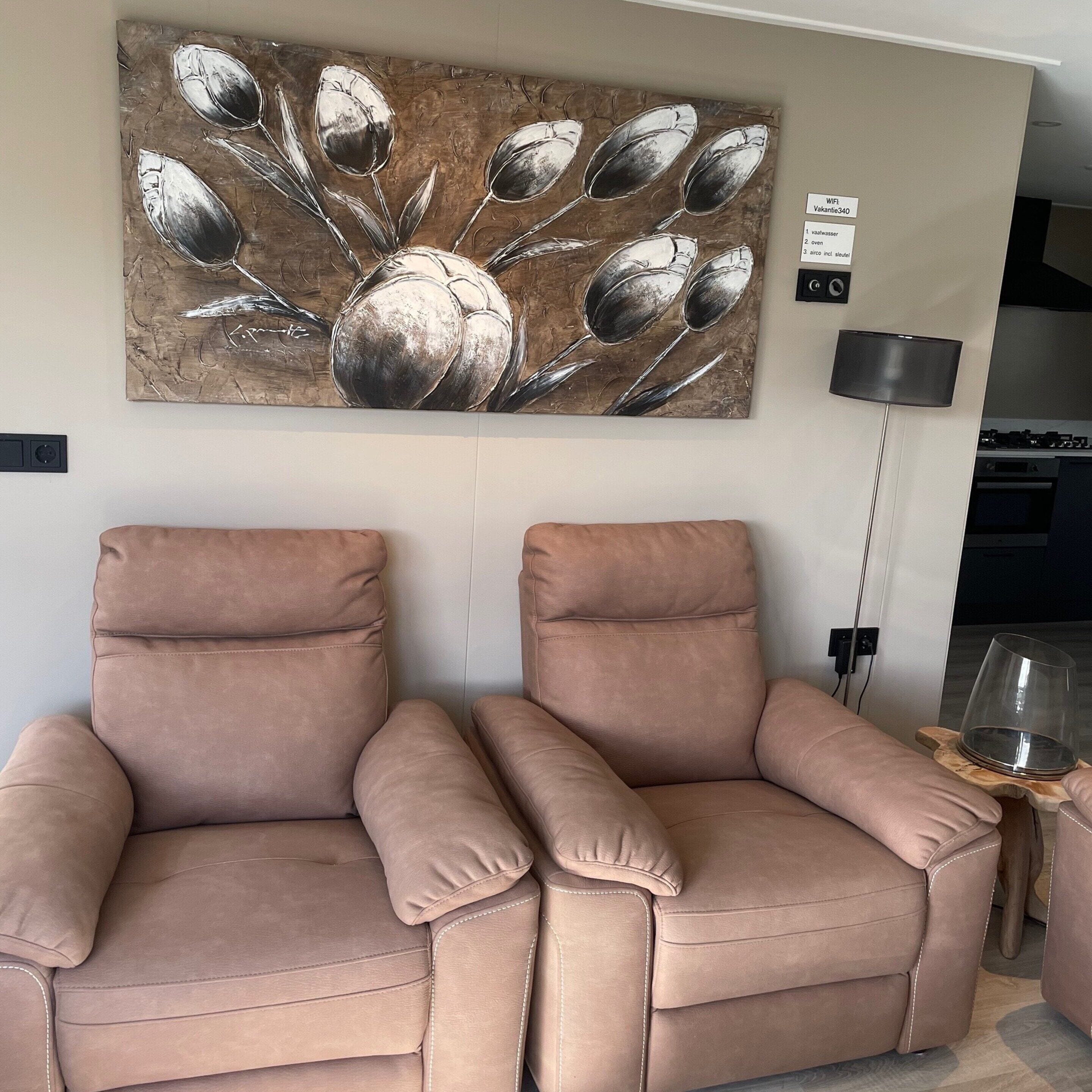A living room with two beige sofas, a large abstract painting, a floor lamp, and a kitchen area in the background.