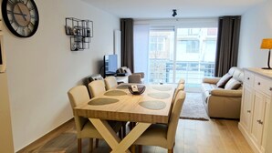Ein modernes Wohnzimmer mit Essbereich, einer Couch, einem Fernseher und einem großen Fenster.