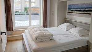 Ein Hotelzimmer mit Bett, einem Fenster mit Vorhängen, einem Bild an der Wand und Blick nach draußen.