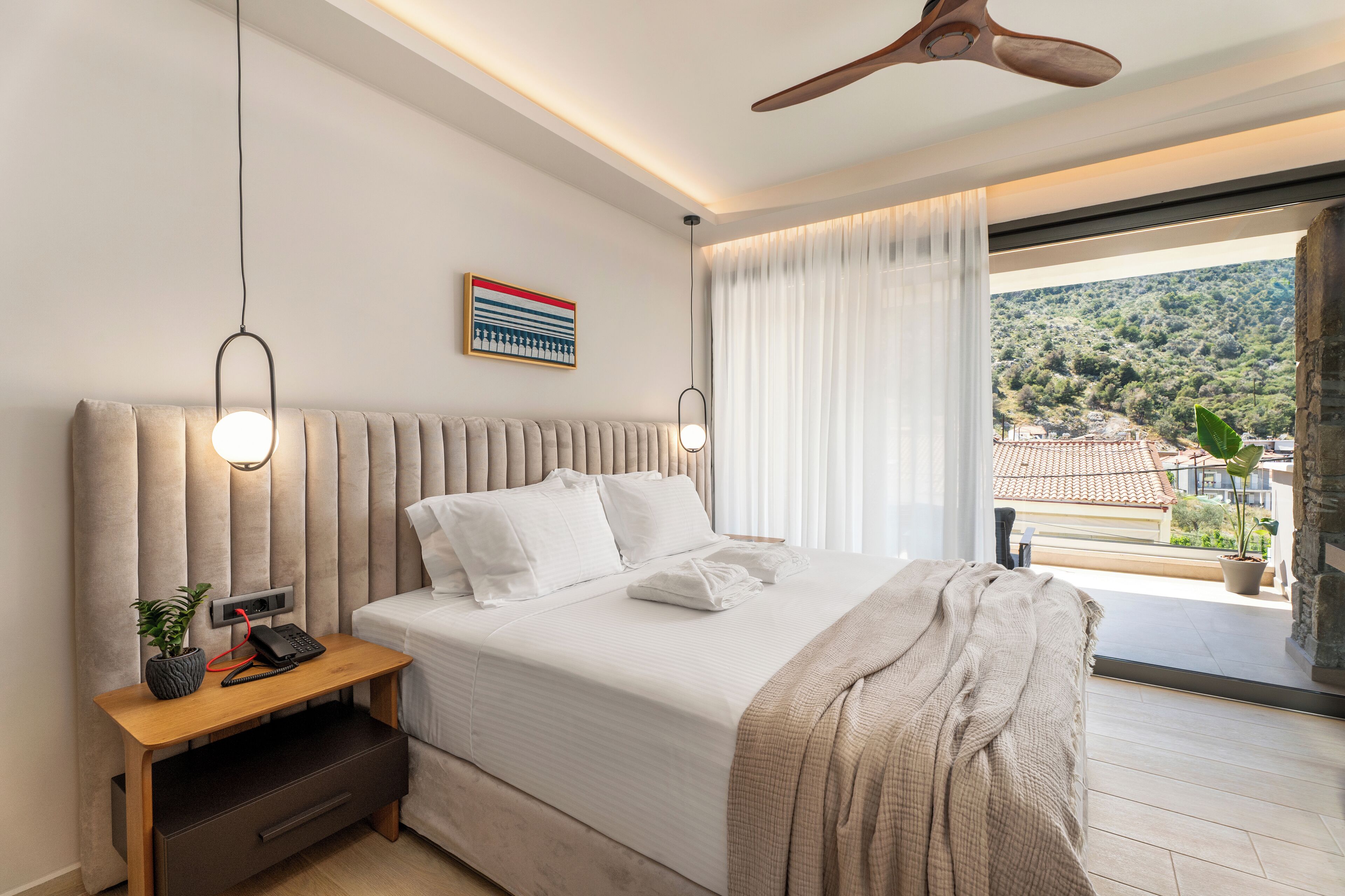 A modern bedroom with a large bed, bedside table with a phone, and a view of a hillside.