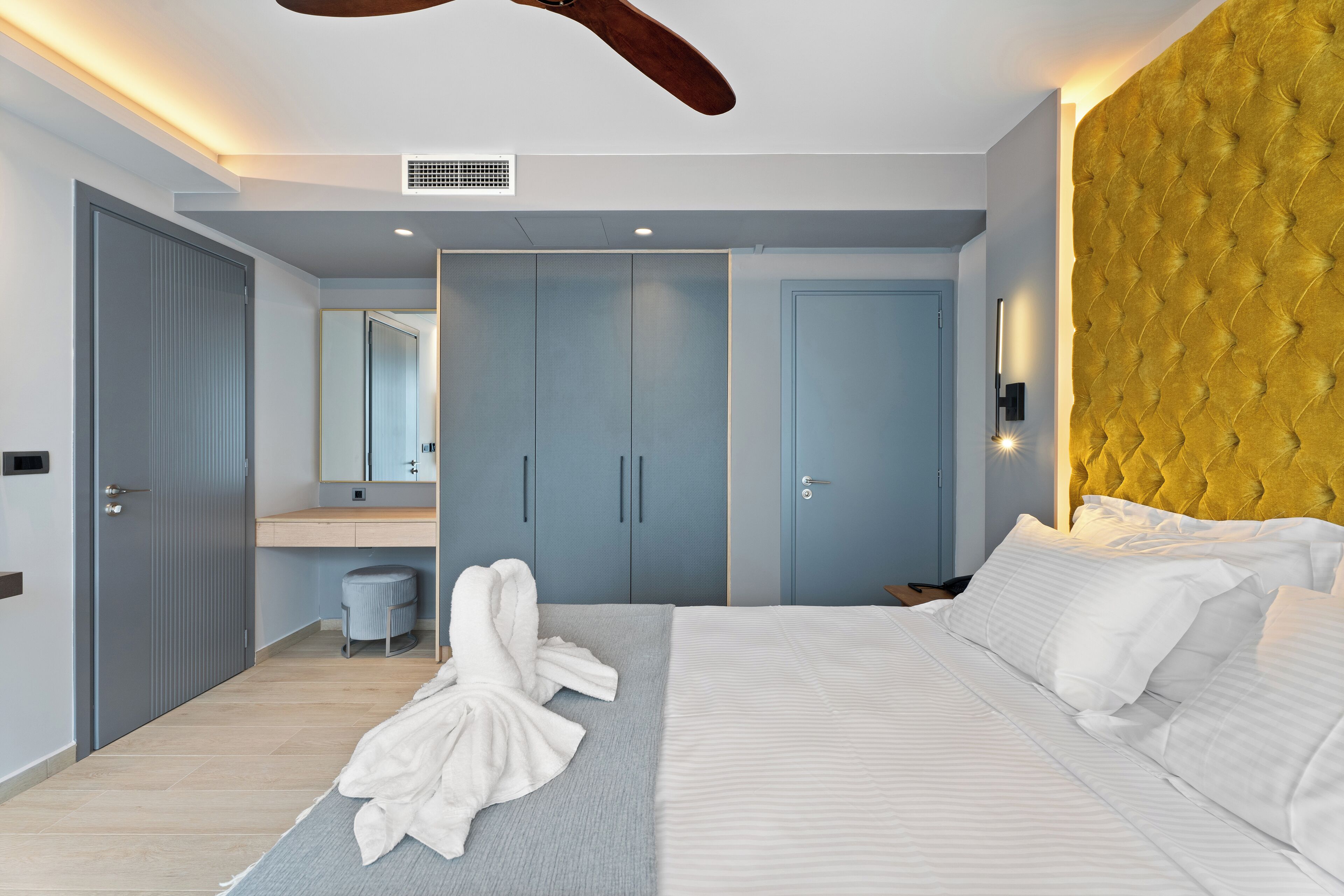 A modern bedroom with a bed, a wardrobe, a mirror, and a ceiling fan.