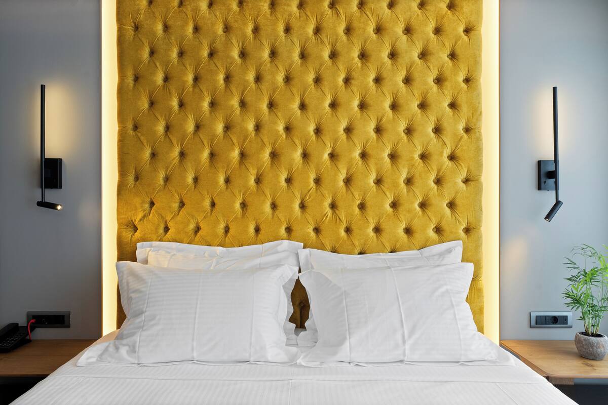 A hotel room with a tufted headboard, white bedding, bedside tables, a phone, and a wall-mounted light fixture.