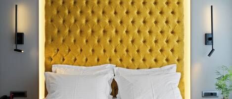 A hotel room with a tufted headboard, white bedding, bedside tables, a phone, and a wall-mounted light fixture.