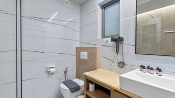 A modern bathroom with a white marble wall, a wooden vanity, a large mirror, and a shower area.