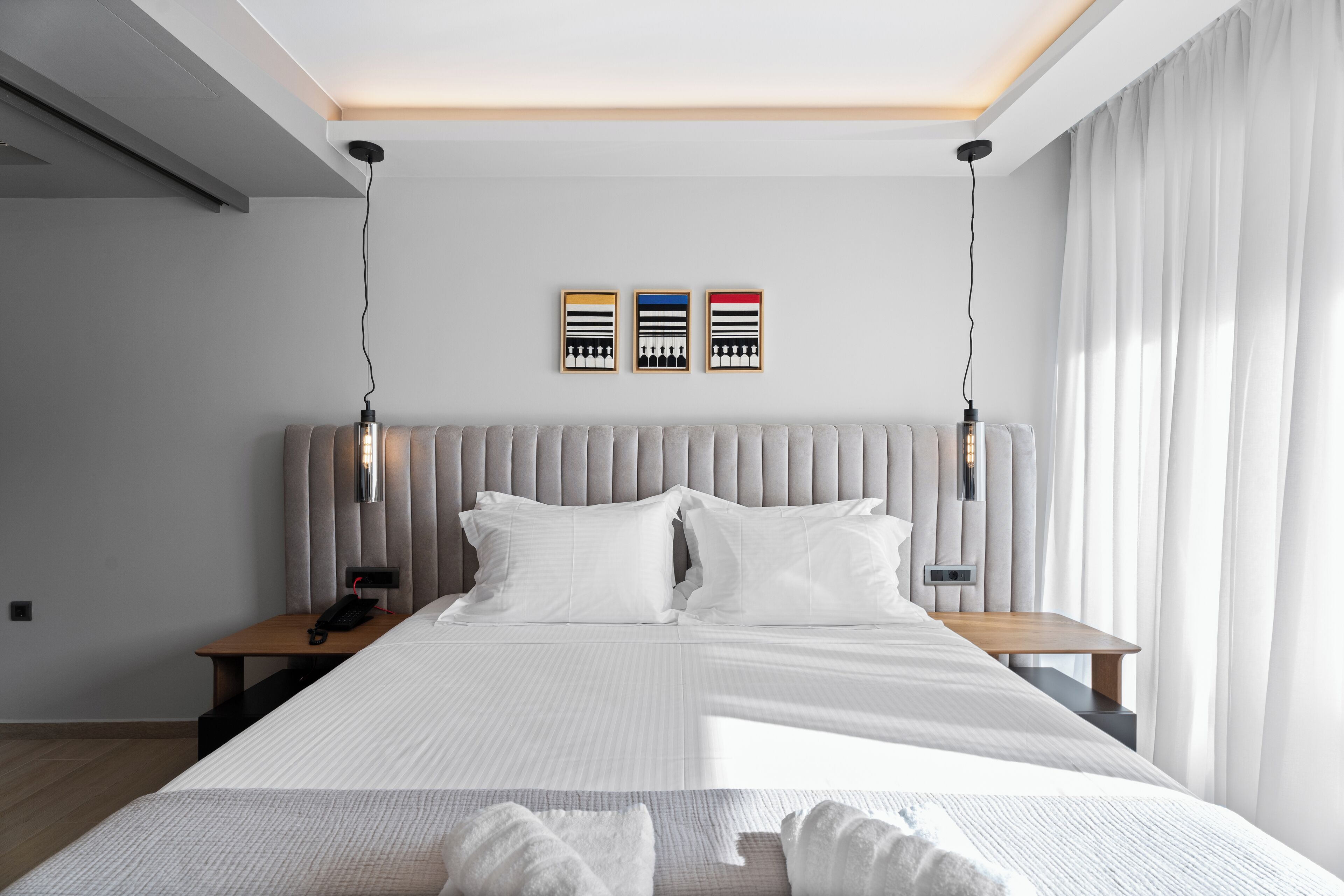 A modern hotel room with a large bed, a bedside table with a phone, and a wall-mounted light fixture.