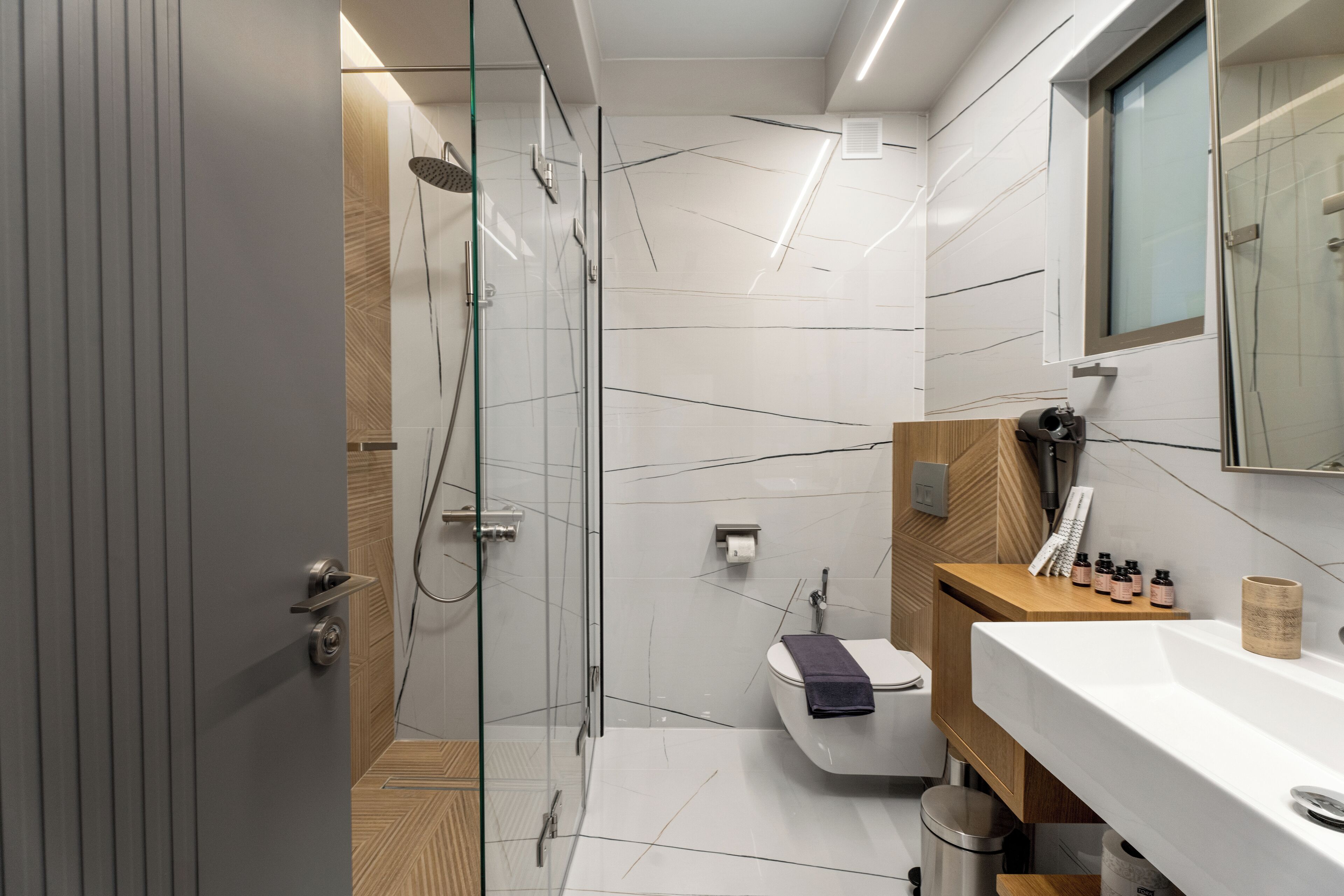 A modern bathroom with a glass shower enclosure, a white sink, and a wooden vanity.