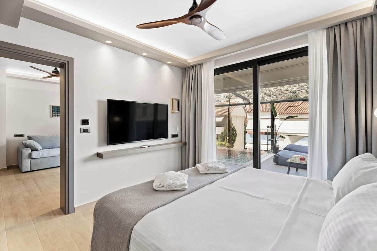 A modern hotel room with a large bed, a flat-screen TV, a ceiling fan, and a view of a pool and outdoor area.