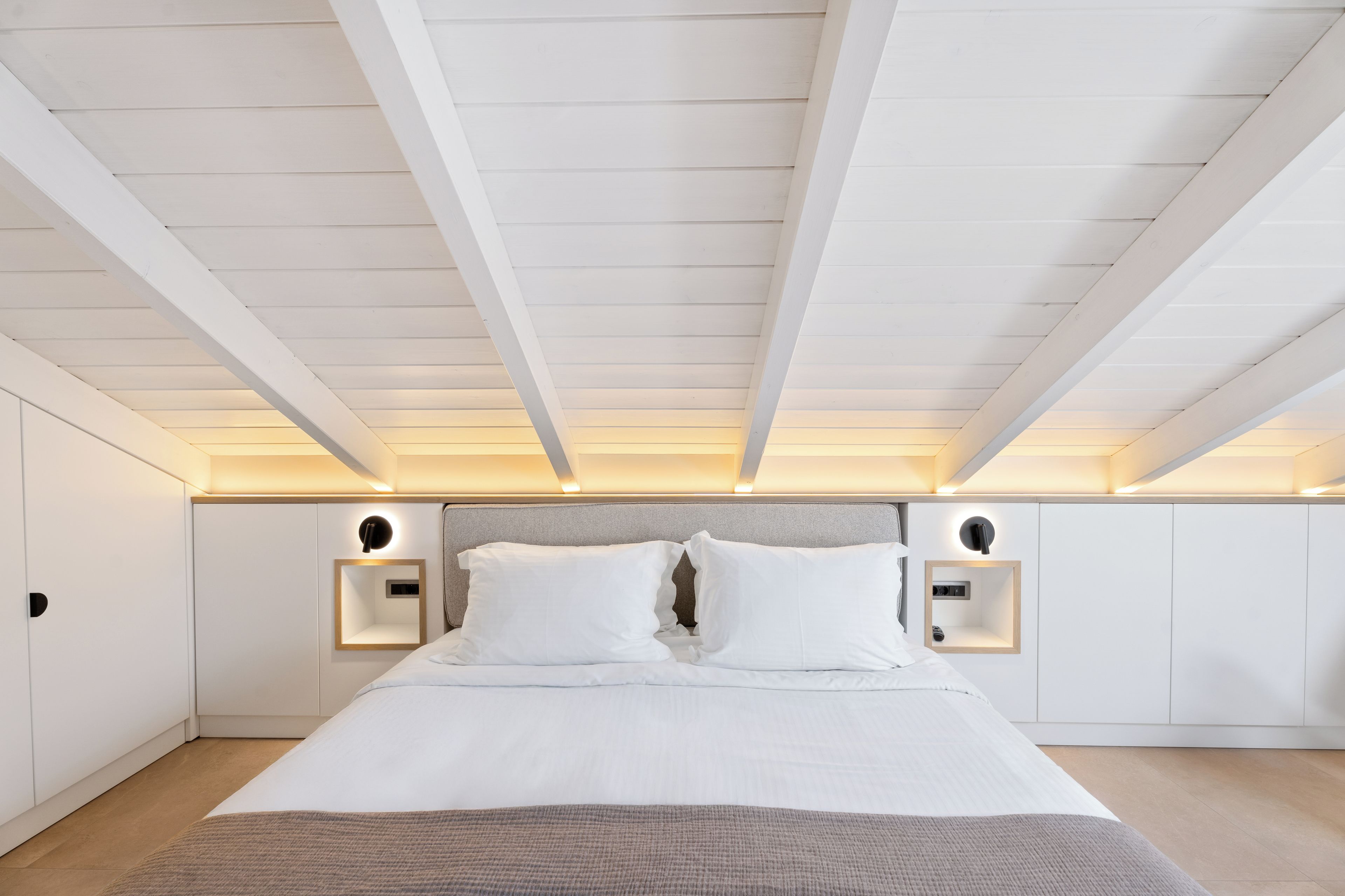 A modern bedroom with a large bed, white walls, and a sloped ceiling with exposed beams.