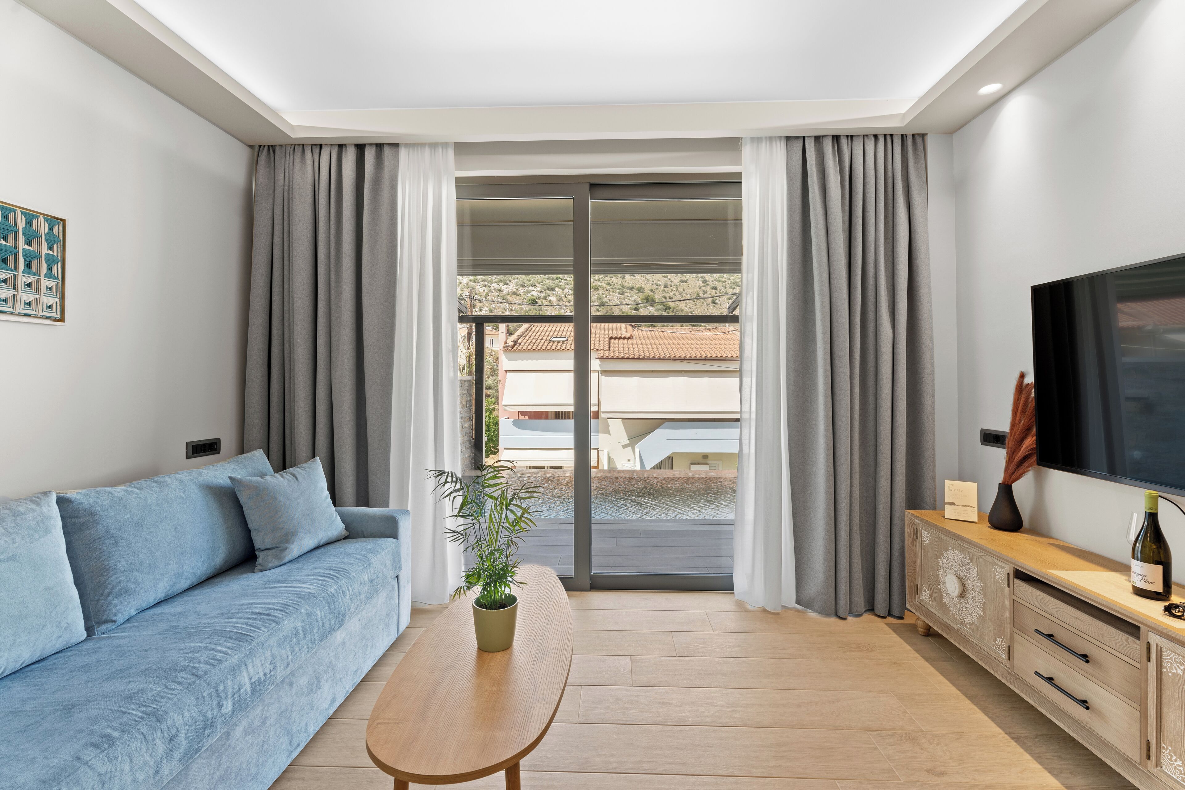 En moderne stue med sofa, sofabord i træ, fjernsyn og skydedør til et udendørs område.