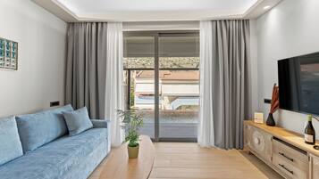 En moderne stue med sofa, sofabord i træ, fjernsyn og skydedør til et udendørs område.