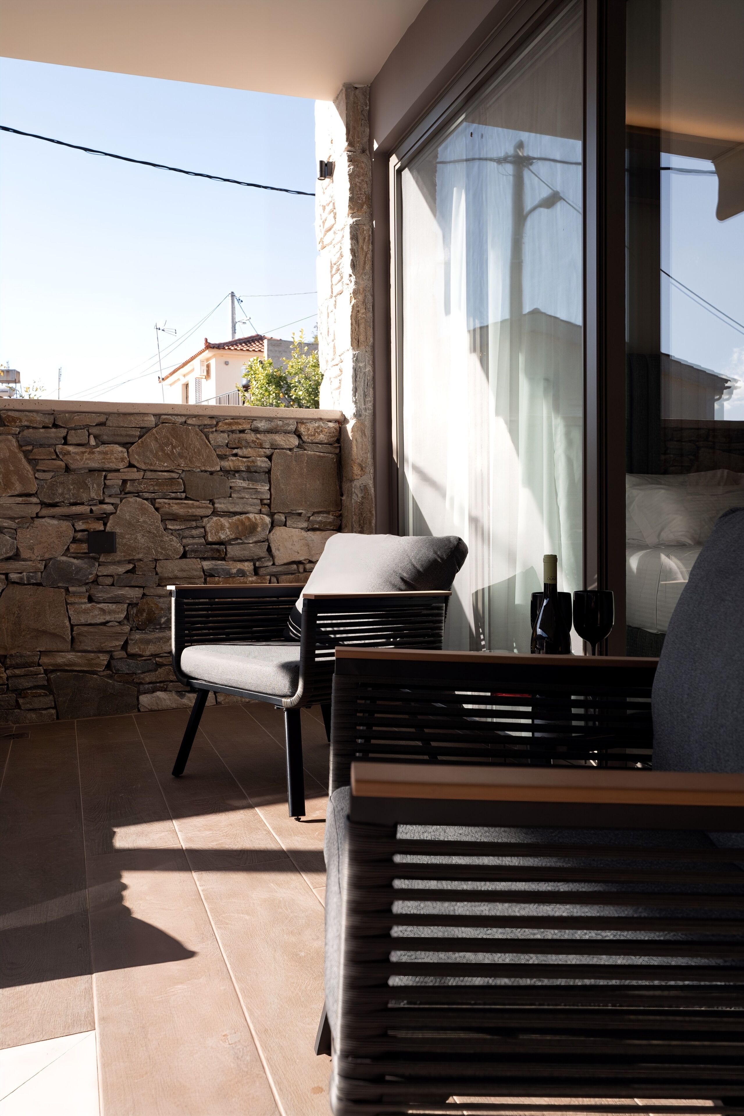 Un balcón con un muro de piedra, una silla acolchada, una mesita y un sofá.