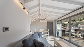 Una sala de estar moderna con un sofá gris, un banco de madera y un ventanal que da a un comedor al aire libre.
