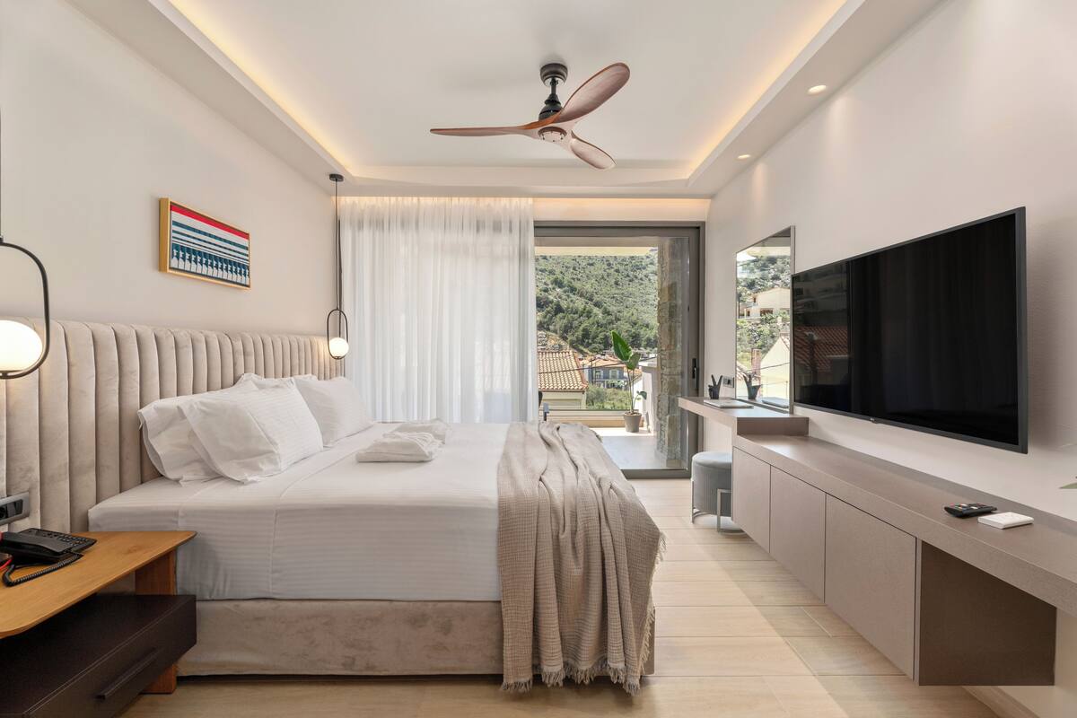 A modern bedroom with a bed, bedside table, TV, and a view of the outdoors.
