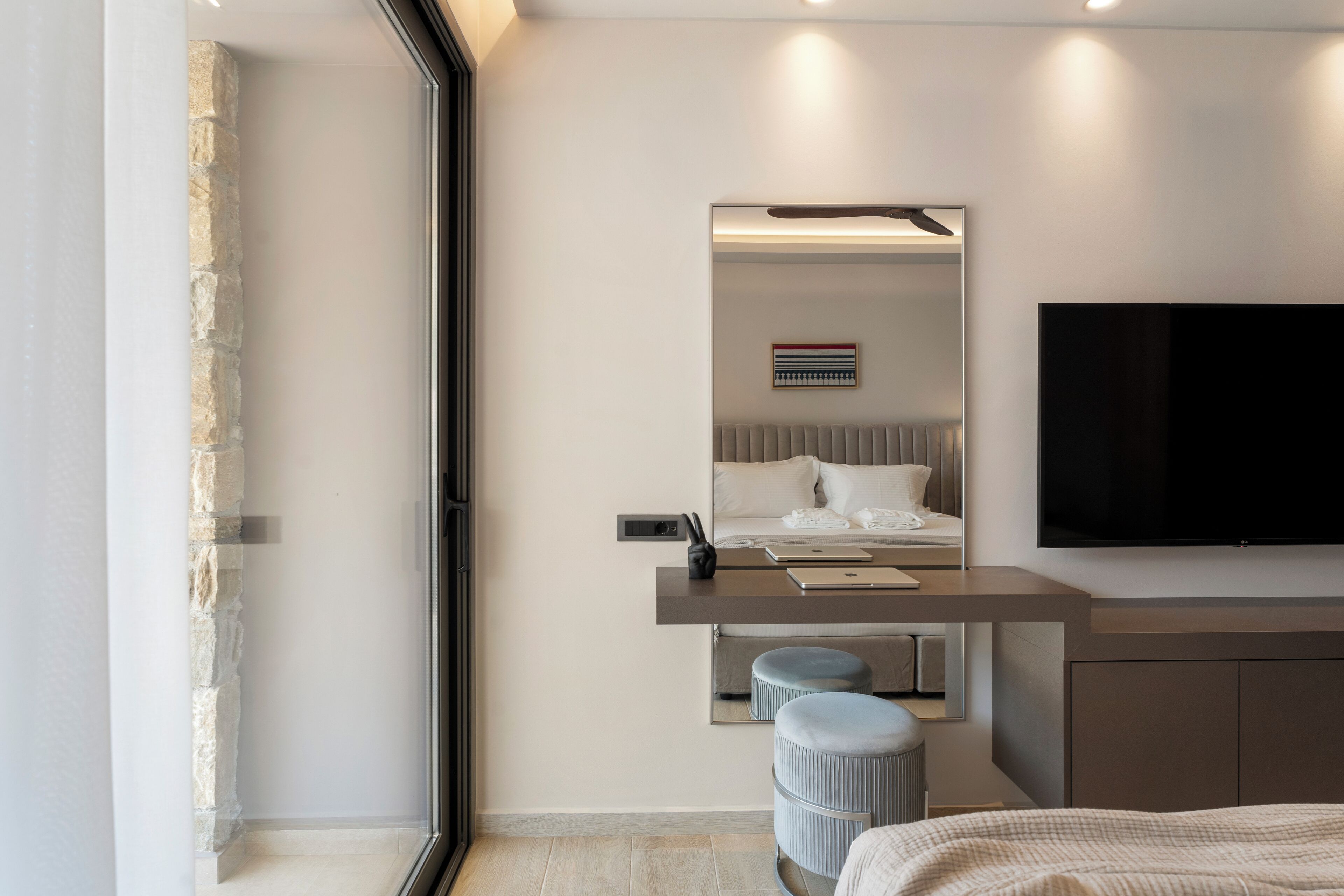 Een moderne slaapkamer met een bed, een bureau, een stoel, een televisie en een groot raam.