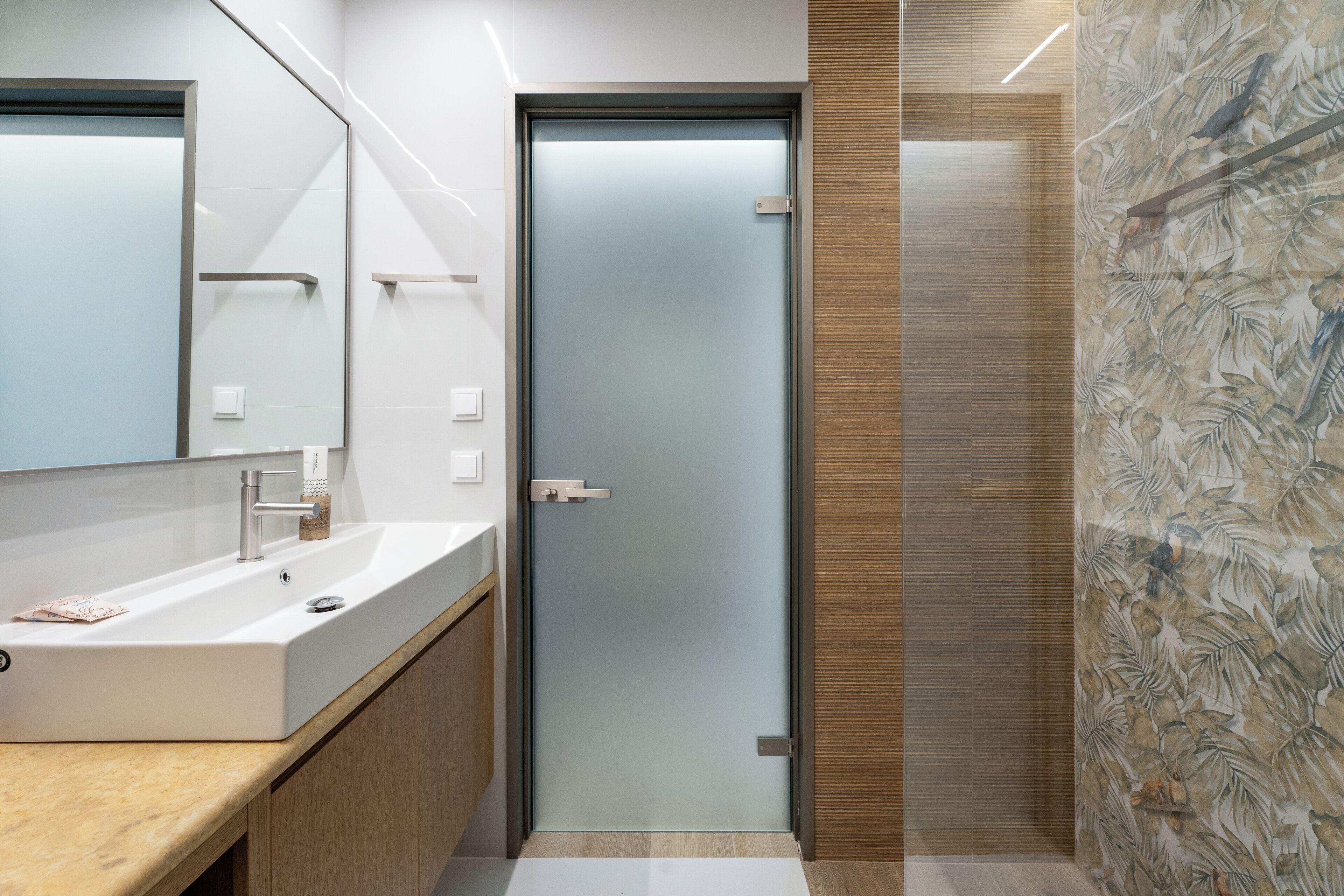 A modern bathroom with a large mirror, a white sink, and a frosted glass door.