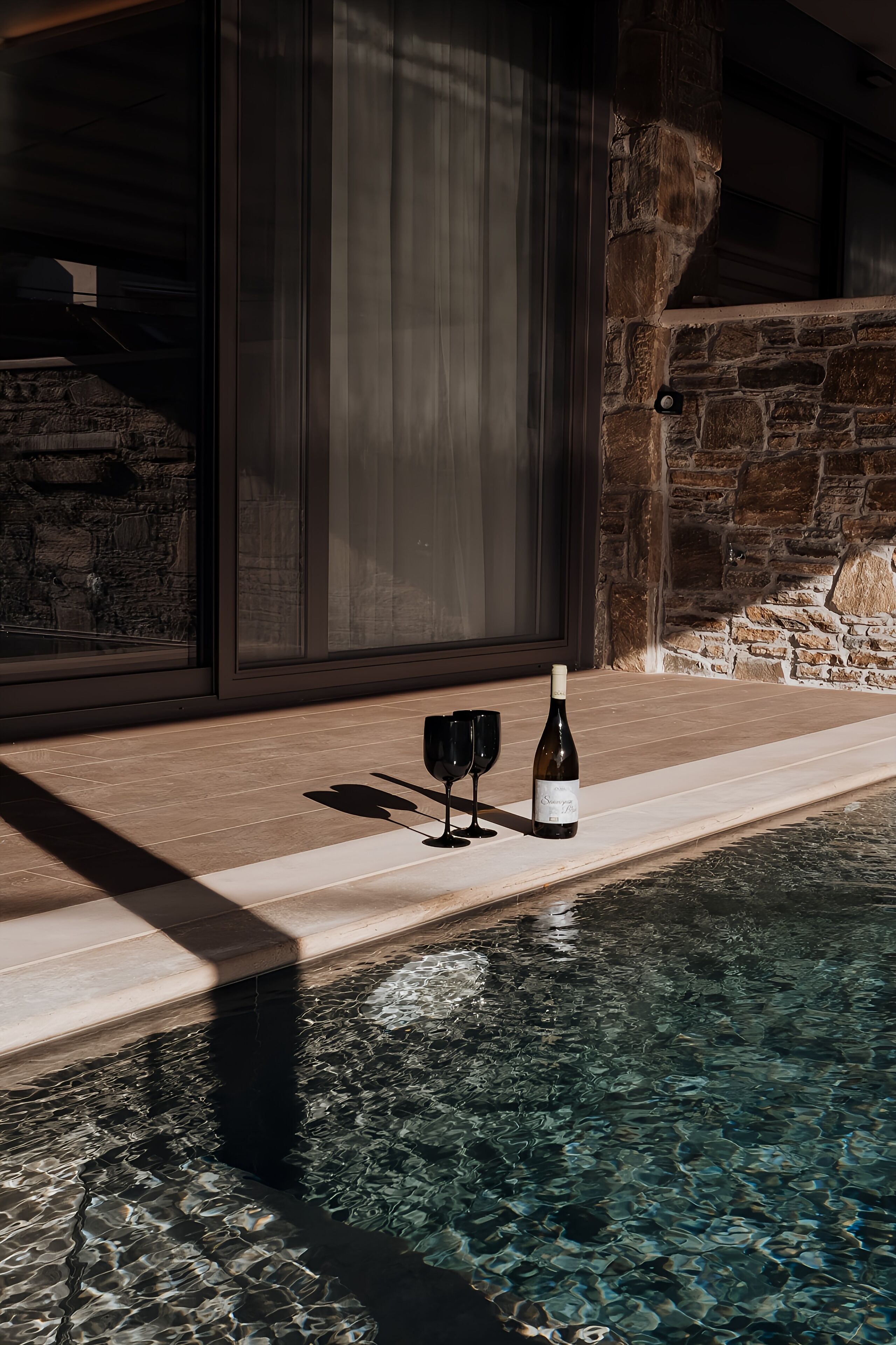 Un área de piscina con un muro de piedra y una puerta de cristal.