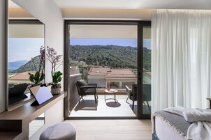 Una habitación de hotel moderna con balcón, un escritorio con una computadora portátil, una silla, una mesita y una cama con una colcha.