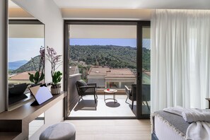 A modern hotel room with a balcony, a desk with a laptop, a chair, a small table, and a bed with a blanket. - Ennea Muses Rooms & Suites (Nafplio)
