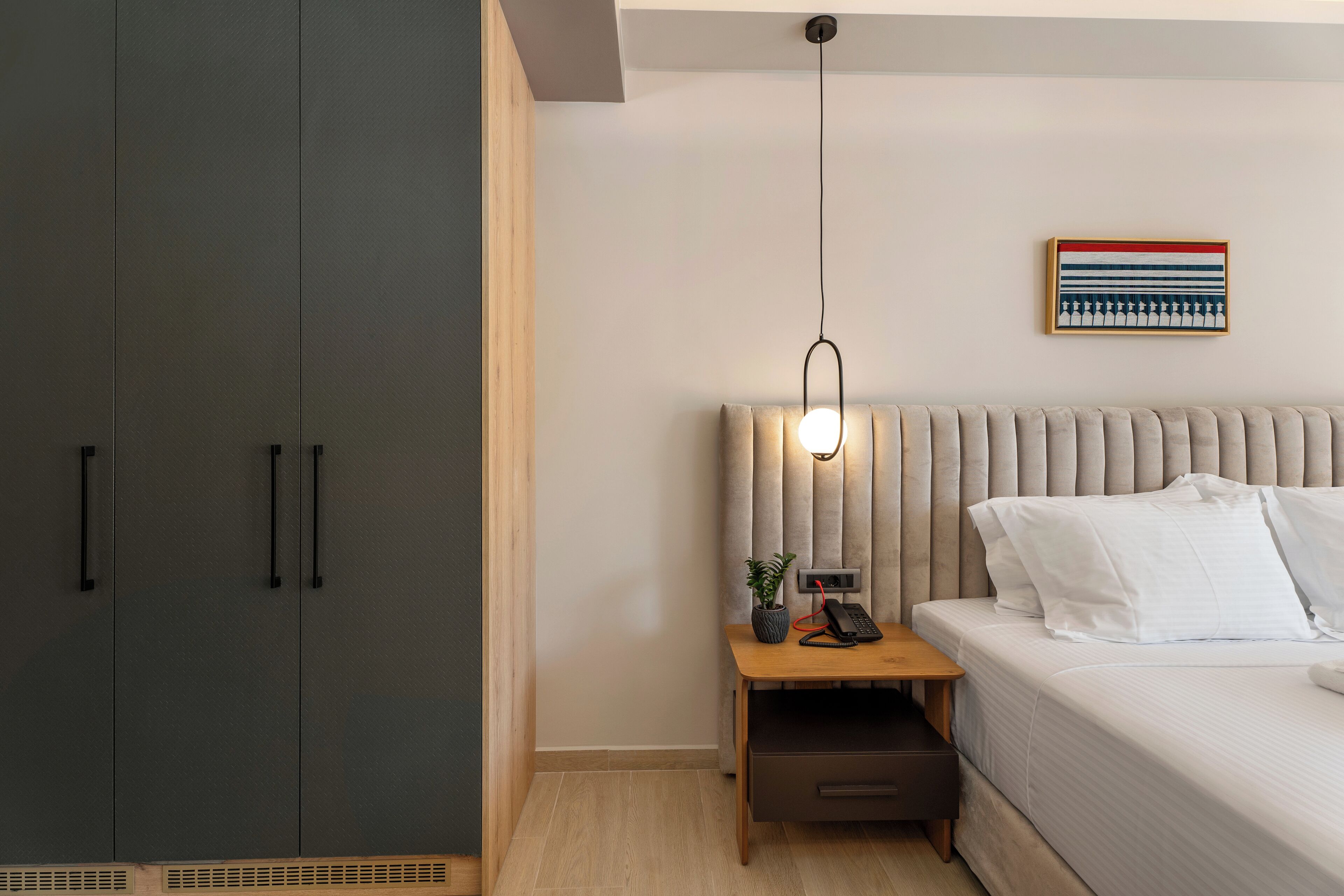 A modern bedroom with a bed, bedside table, lamp, and a wall-mounted artwork.