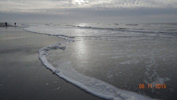 A beach with waves and a few people in the distance. - Ferienhaus Fischerkate (St. Peter-Ording)