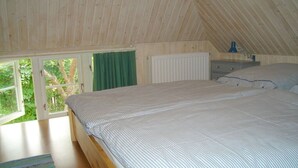 Een slaapkamer met een schuine plafond, een groot bed, een raam met gordijnen en een radiator.