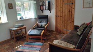 A cozy living room with a leather chair, a brown sofa, a bookshelf, and a wooden door. - Ferienhaus Fischerkate (St. Peter-Ording)