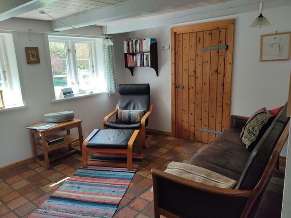 Una sala de estar acogedora con un sillón de cuero, un sofá marrón, una estantería y una puerta de madera.