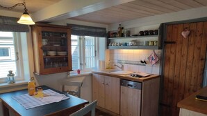 A kitchen with wooden cabinets, a sink, and a dining table with chairs. - Ferienhaus Fischerkate (St. Peter-Ording)