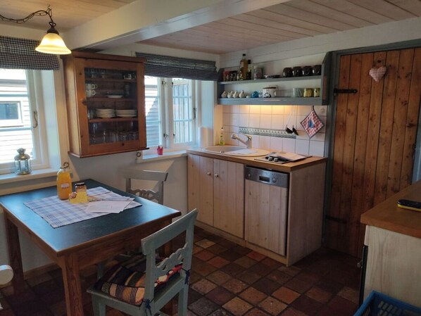 A kitchen with wooden cabinets, a sink, and a dining table with chairs. - Ferienhaus Fischerkate (St. Peter-Ording)