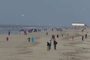A beach with people walking and standing, a lifeguard tower, and a clear sky. - Ferienhaus Fischerkate (St. Peter-Ording)