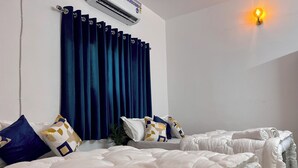 A hotel room with two beds, dark blue curtains, white bedding, and a wall-mounted air conditioner. - Rangoon by Grehstay 2BHK Independent House near Expo Mart (Greater Noida)