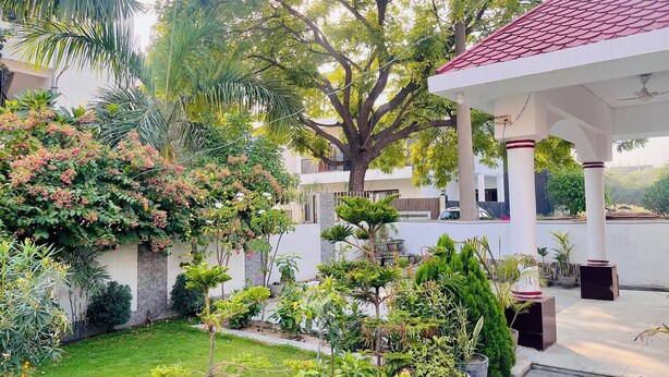 A covered outdoor area with a lawn, potted plants, and a large tree. - Rangoon by Grehstay 2BHK Independent House near Expo Mart (Greater Noida)