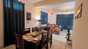 A dining area with a table set for four, a sofa set, and a potted plant. - Rangoon by Grehstay 2BHK Independent House near Expo Mart (Greater Noida)