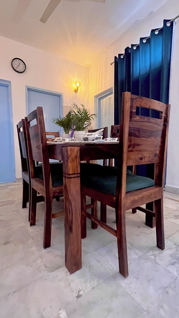 Un comedor con una mesa y sillas de madera, un reloj en la pared y una ventana con cortinas.