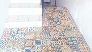 Una escalera con escalones blancos que lleva a una puerta oscura. El piso está cubierto de patrones coloridos.