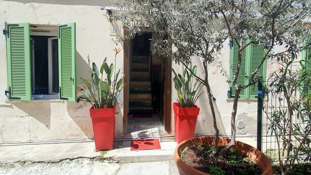 Una entrada de edificio con contraventanas verdes, una escalera azulejada y plantas en macetas.
