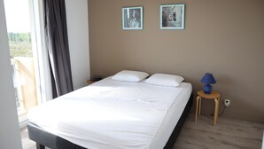 Ein Schlafzimmer mit einem großen Bett, zwei Kissen, einem Nachttisch mit Lampe und zwei gerahmten Bildern an der Wand.